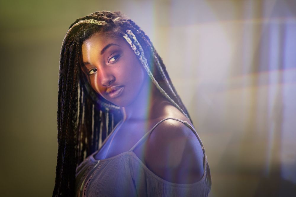 Artistic portrait with long braids and bare shoulders against atmospheric lighting.