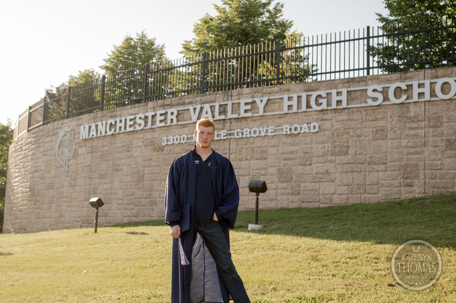 Graduate posing in front of Manchester Valley High School stone entrance wall.