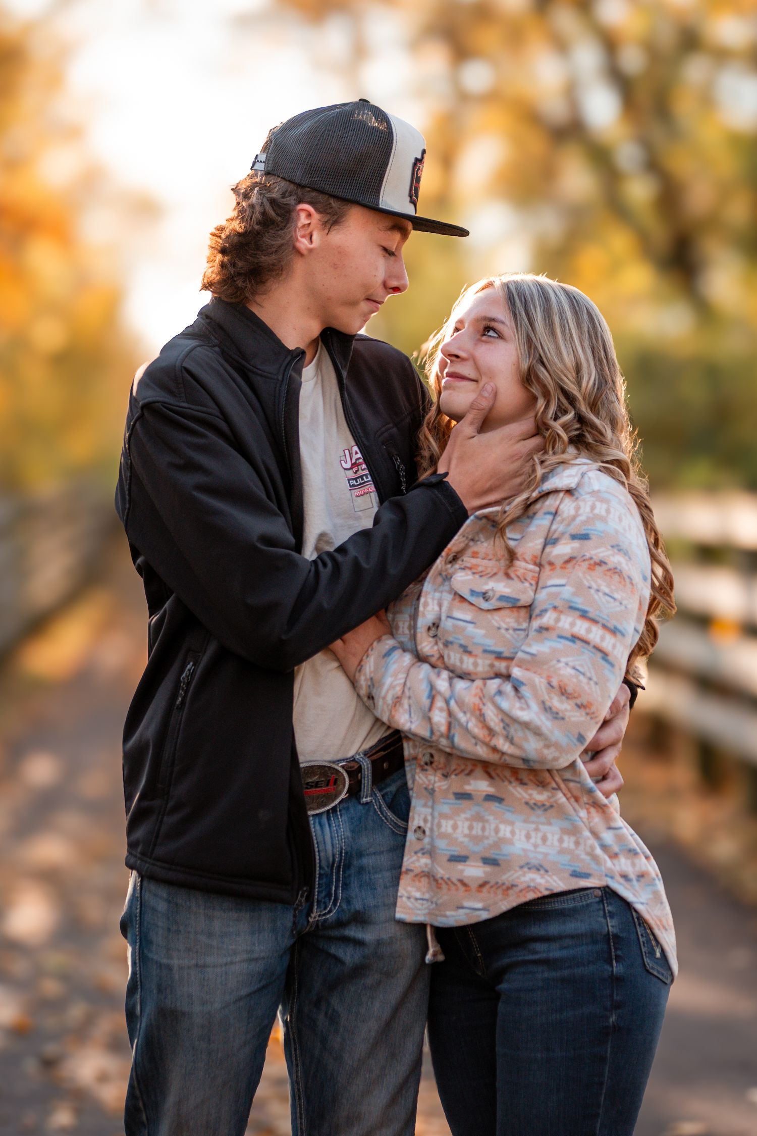 A loving couple shares a tender moment outdoors during autumn with golden foliage in the background.