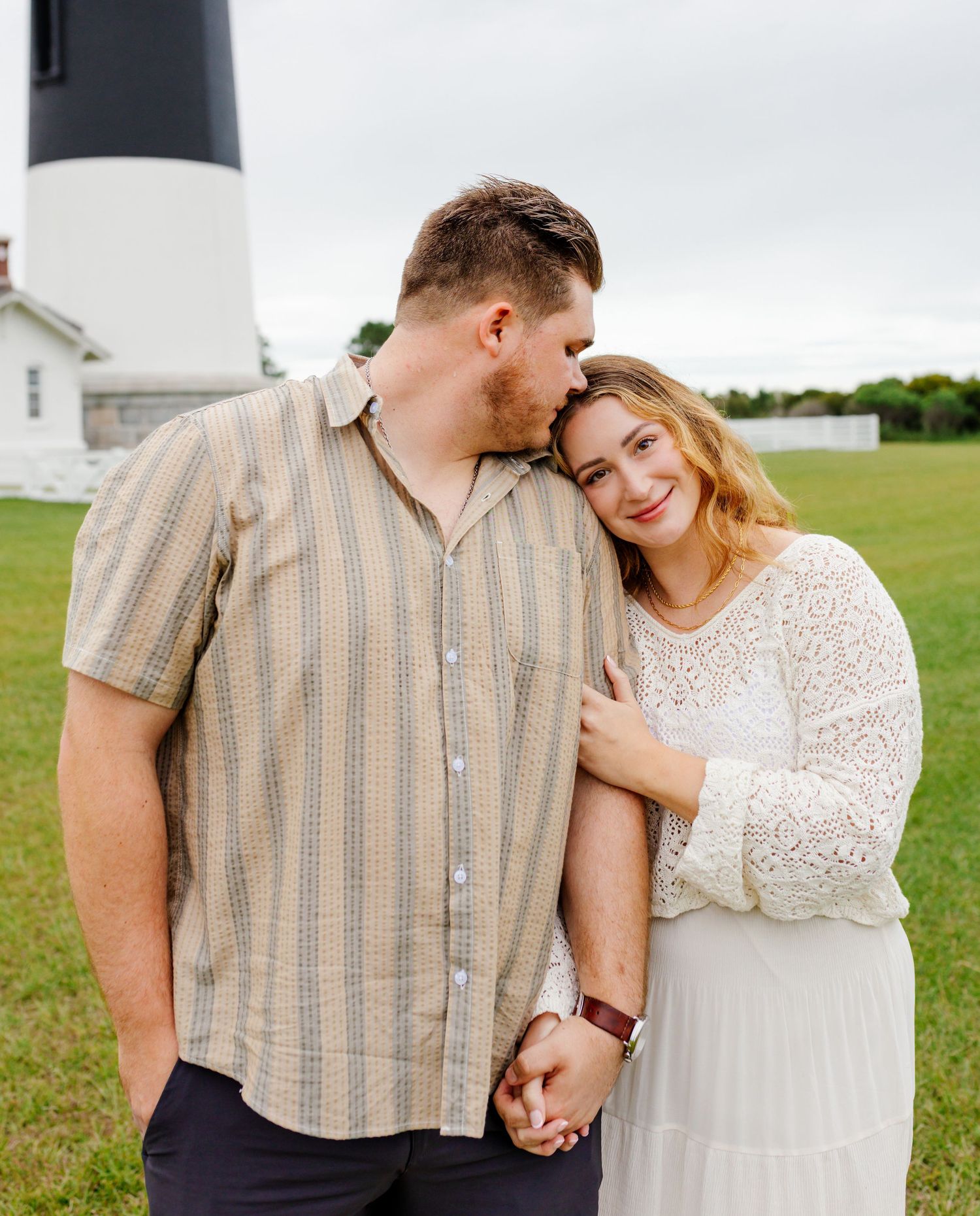 Romantic couple in vintage-inspired outfits pose together near a lighthouse.