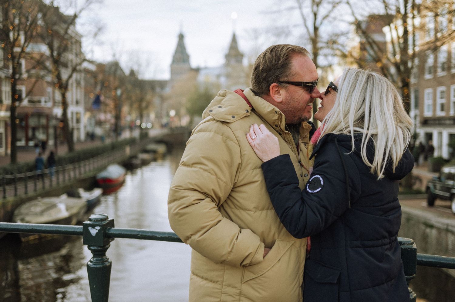 A romantic couple sharing an intimate moment on a bridge in Amsterdam with historic architecture in the background.
