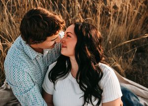 Couple sharing a tender almost-kiss moment while sitting in a sun-kissed wheat field. Couple photography. Engagement photos.