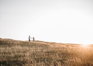 Two people holding hands silhouetted on golden hillside meadow during stunning sunset. Couple photography. Engagement photos.