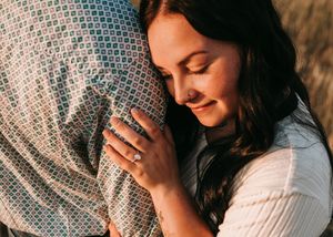 Woman smiling contentedly while embracing partner, showing elegant engagement ring closeup. Couple photography. Engagement photos.