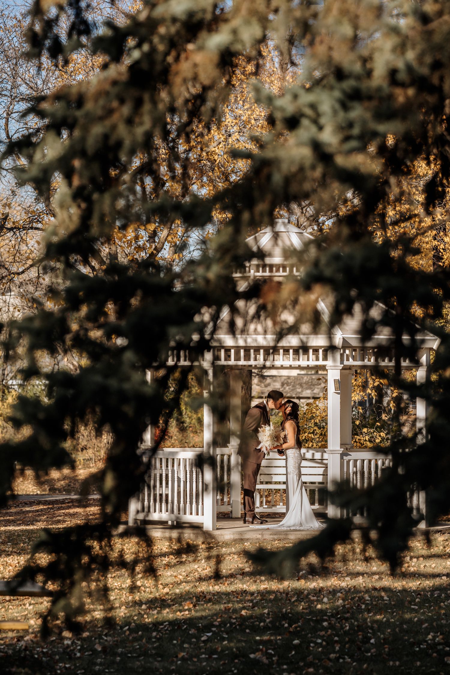 Wedding couple sharing a tender moment inside a white gazebo surrounded by autumn trees.