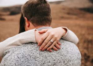 Close-up of a woman showing her diamond engagement ring while embracing her partner outdoors. Couple photography. Engagement photos.
