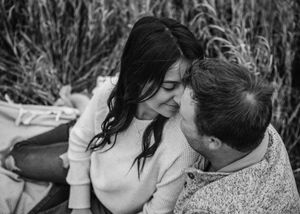 Black and white photo of a couple sharing a tender moment, smiling together in a field of tall grass. Couple photography. Engagement photos.
