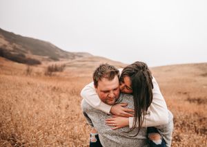 Happy couple embracing in a golden field, woman kissing mans cheek during outdoor engagement session. Couple photography. Engagement photos.