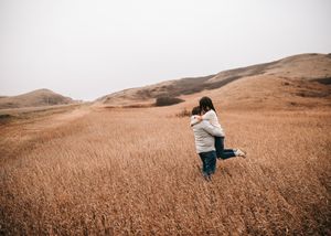 Woman twirling joyfully in a vast golden wheat field with rolling hills in the background. Couple photography. Engagement photos.