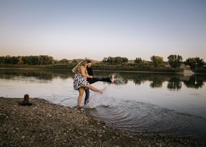 Couple playfully splashing in a shallow river at dusk, laughing and enjoying their engagement photo session. Engagement photos.