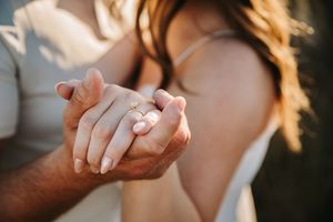 Close-up of couple holding hands showing engagement ring in soft natural outdoor lighting. Engagement photos.