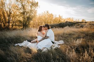 Couple sharing a romantic kiss while sitting in a golden field of tall grass during sunset. Engagement photos.