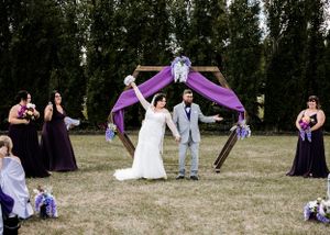 Bride and groom celebrating under a purple draped hexagonal arch during outdoor wedding ceremony.