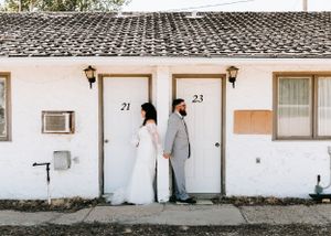 Bride and groom holding hands in front of a white motel wall with numbered doors 21 and 23.