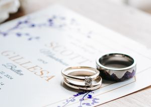 Diamond engagement ring and mountain-themed wedding band resting on floral wedding invitation.