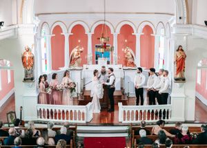 Wedding ceremony at a pink and white church altar with bride, groom, and wedding party standing together.