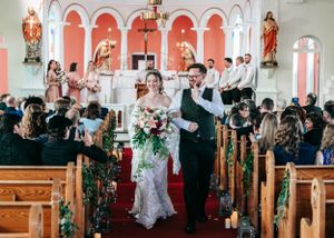 Newlyweds walk down the aisle together as guests celebrate in a beautiful pink church.