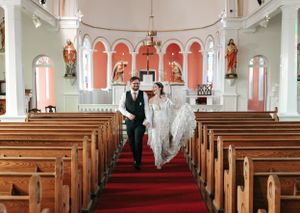 Bride and groom walk hand in hand down the red carpet aisle of a white church.