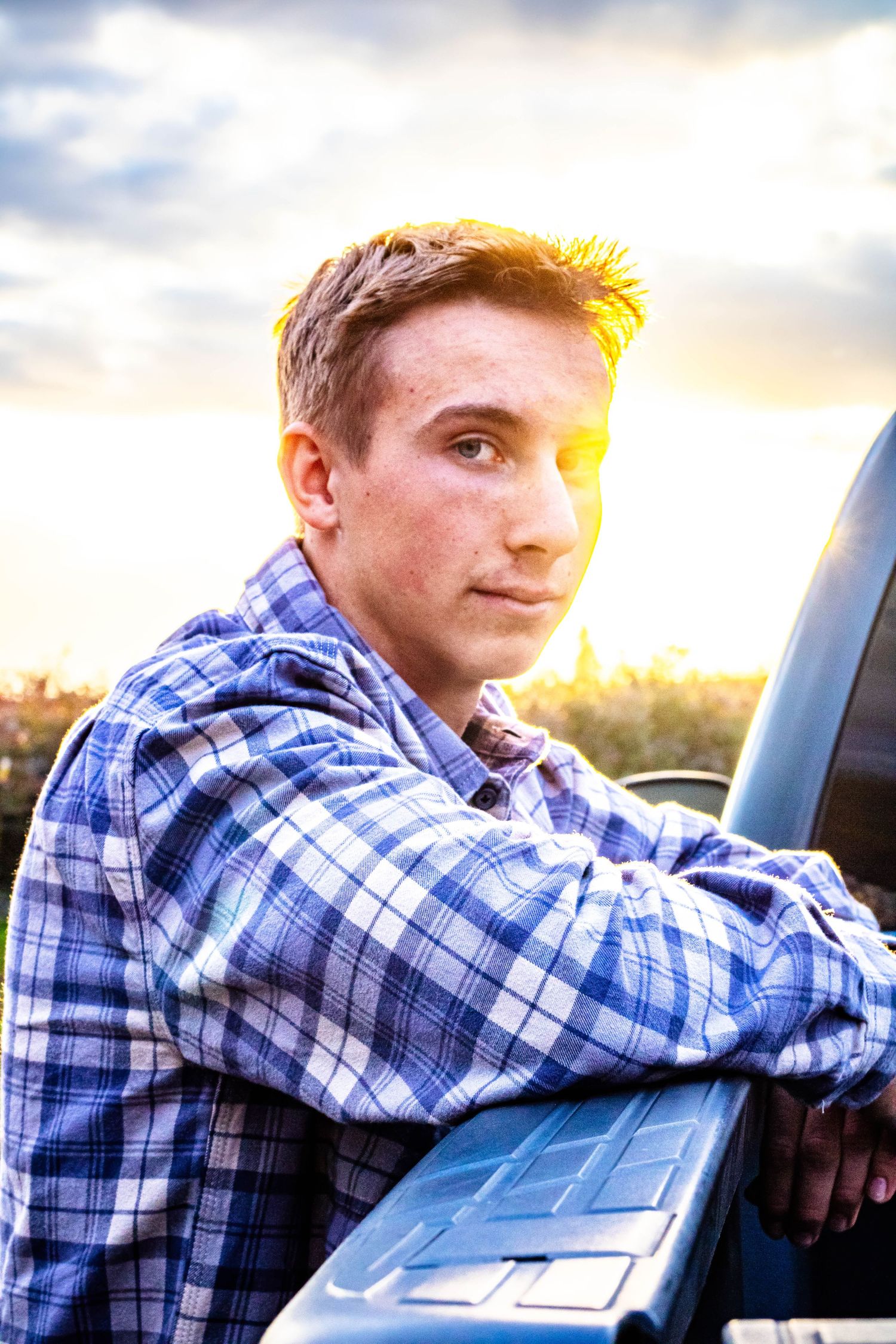 young man leans against truck and looks at the camera as the sun shines over his shoulder