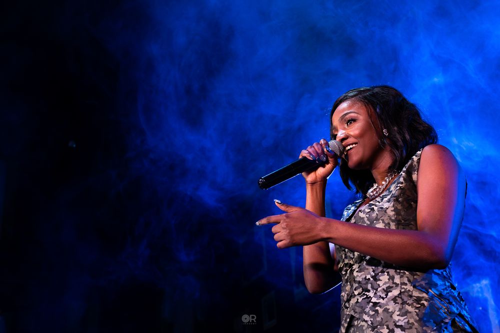 A singer performs passionately on stage against a dramatic blue-lit backdrop with smoke effects.