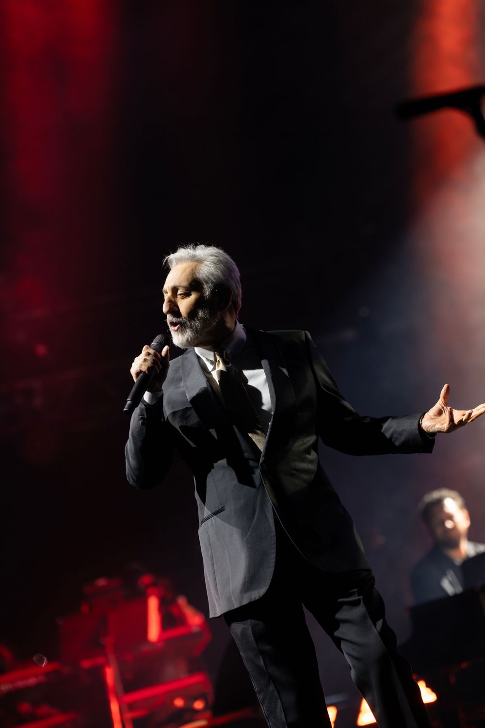 Performer in dark suit silhouetted against dramatic red stage lighting.