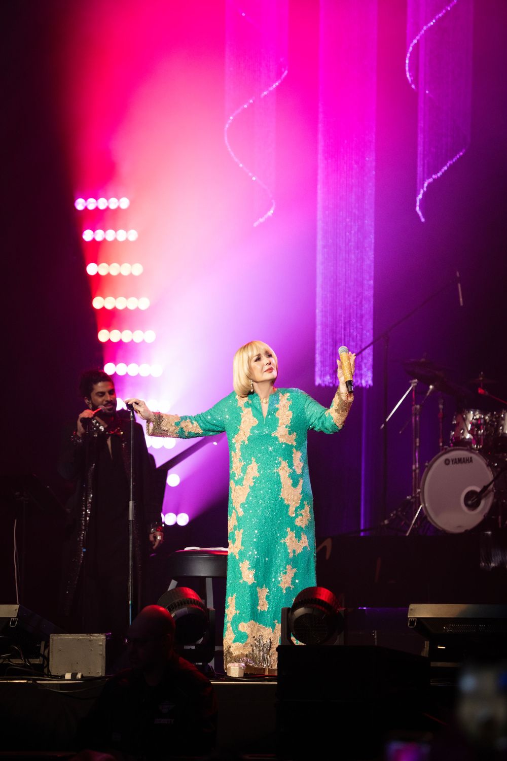 Stage performance with vibrant pink and purple lighting featuring green sequined costume.
