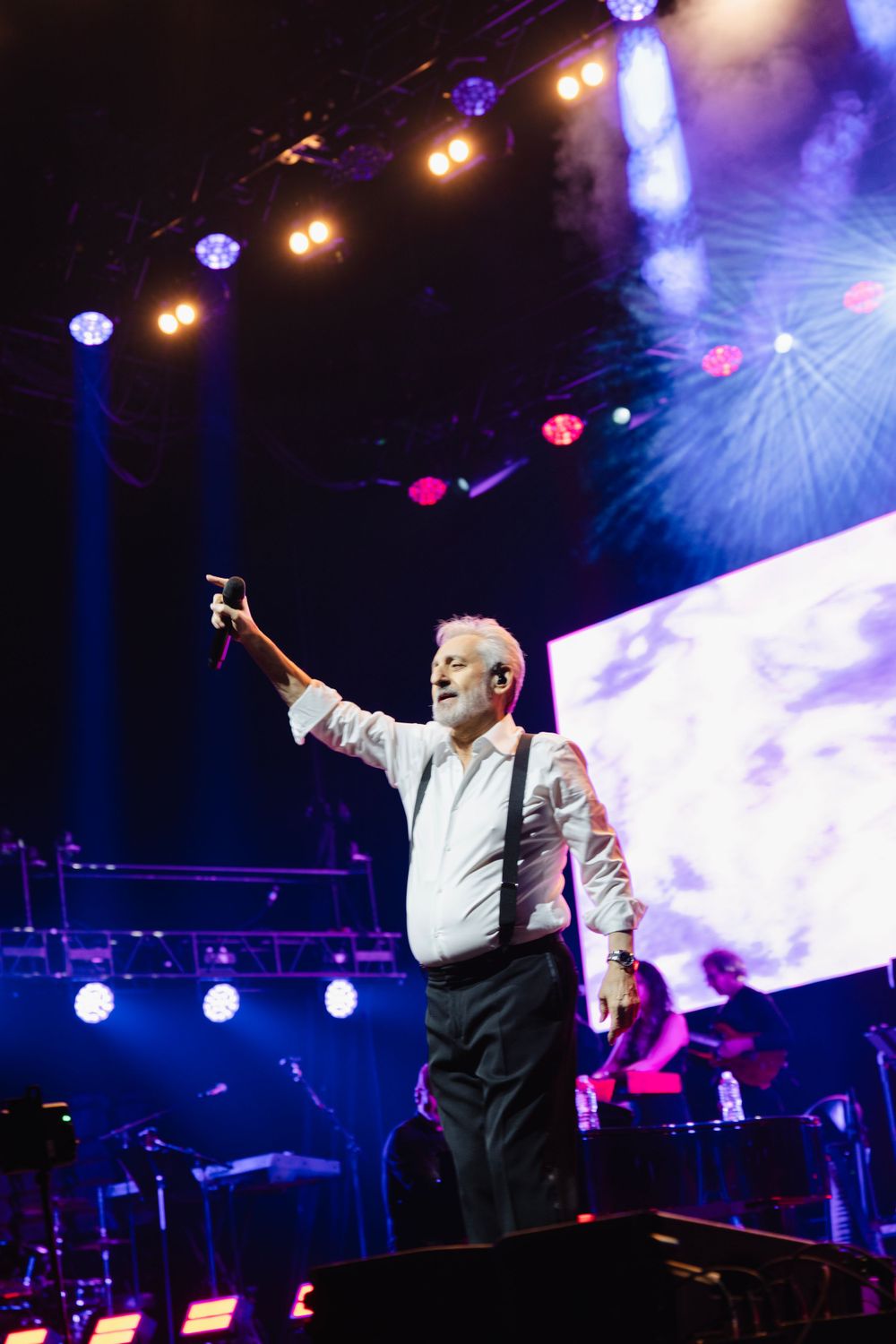 Concert performer in white shirt under dramatic blue and purple stage lighting.