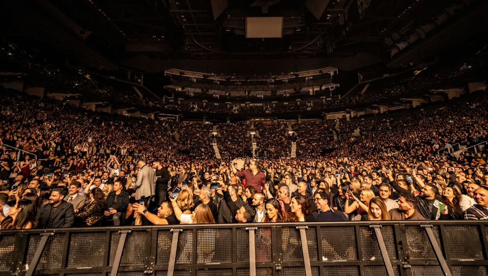 Panoramic view of a packed arena concert venue filled with audience members.