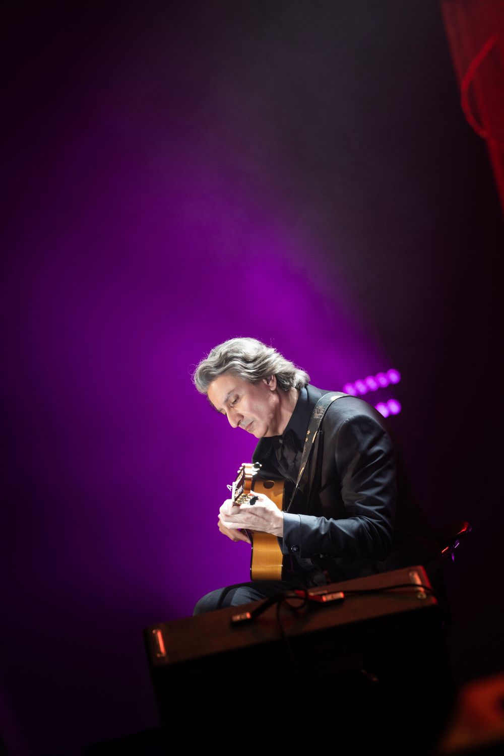Musician performing on acoustic guitar under purple stage lighting in dramatic silhouette.