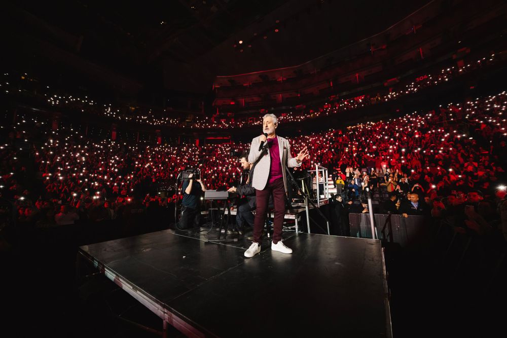 Wide shot of concert arena with red lighting and illuminated crowd.