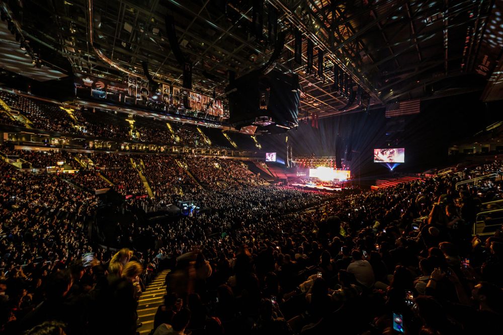Panoramic view of arena concert showing stage and audience under dramatic lighting.
