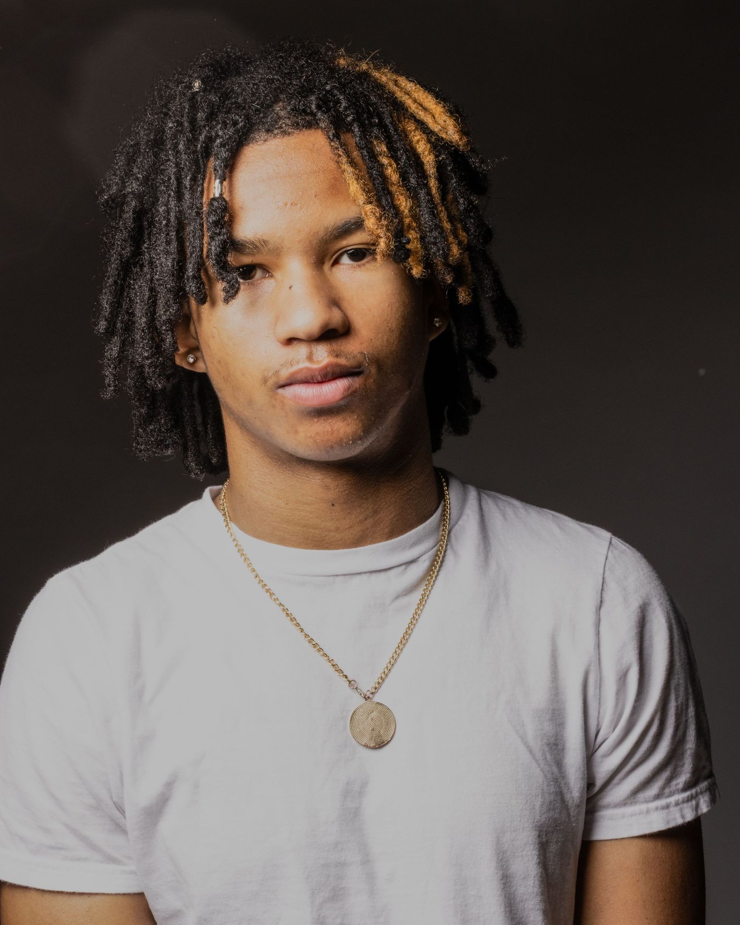 Portrait of Jaden with the dark background with him wearing a gray shirt and gold necklace