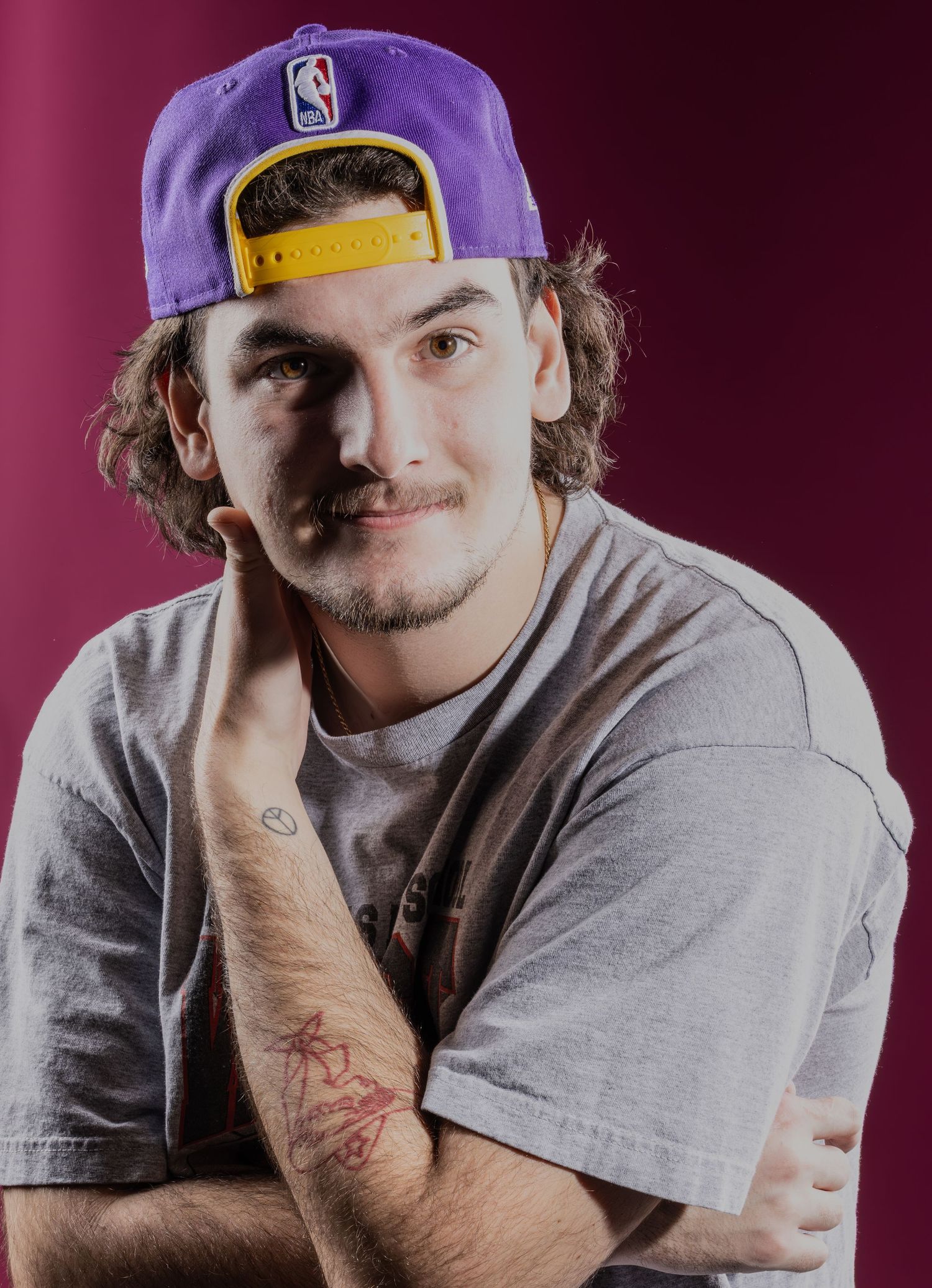 Portrait of Wes wearing a gray shirt, purple hat with yellow band