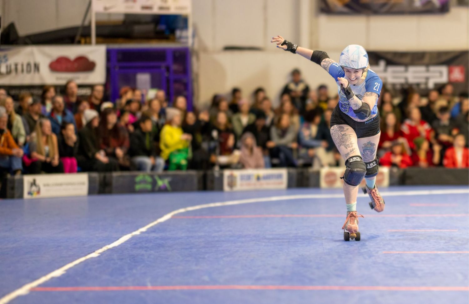 Roller derby skater races around the track with a blurred crowd watching in the background.