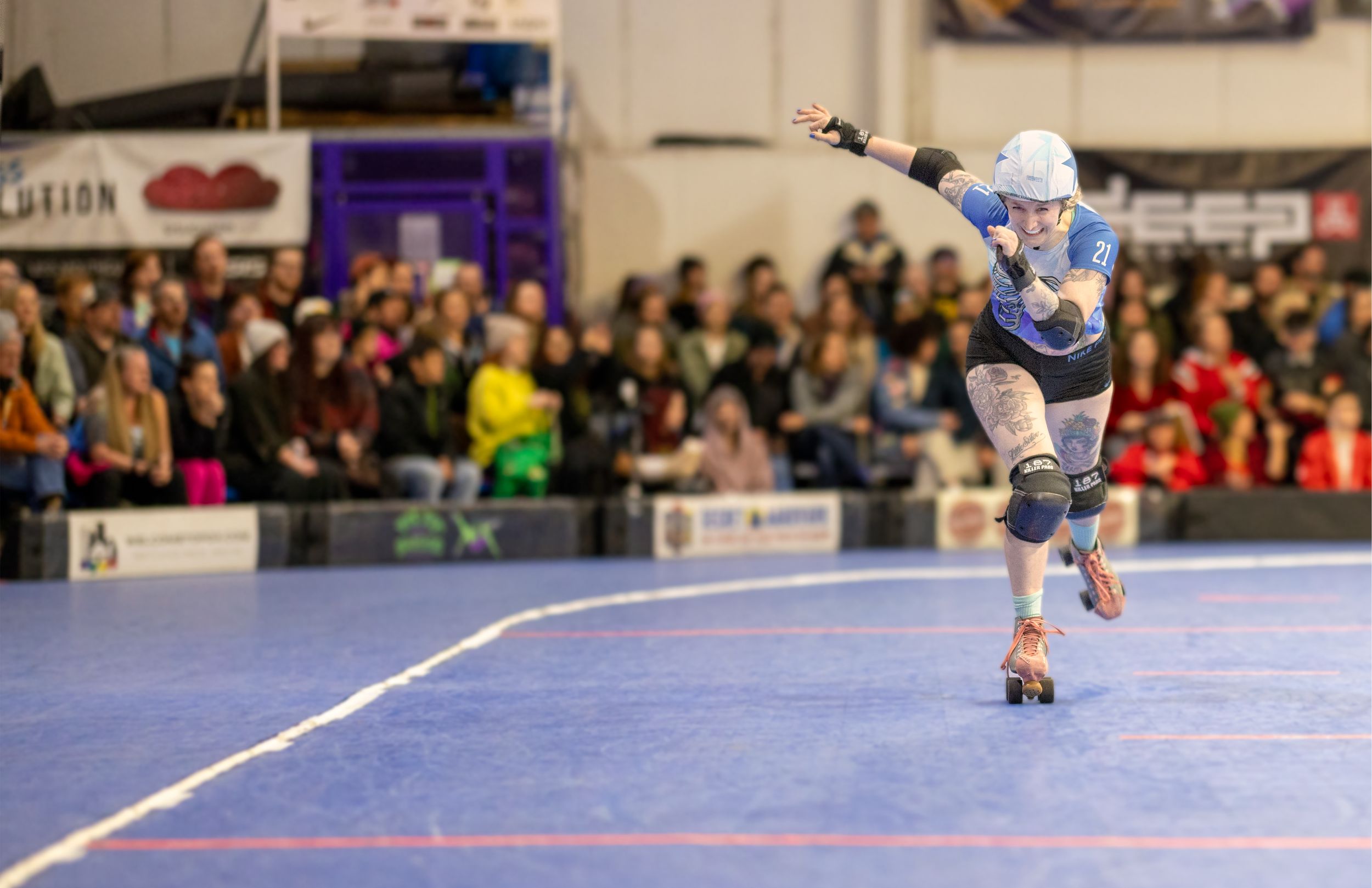 Roller derby skater races around the track with a blurred crowd watching in the background.