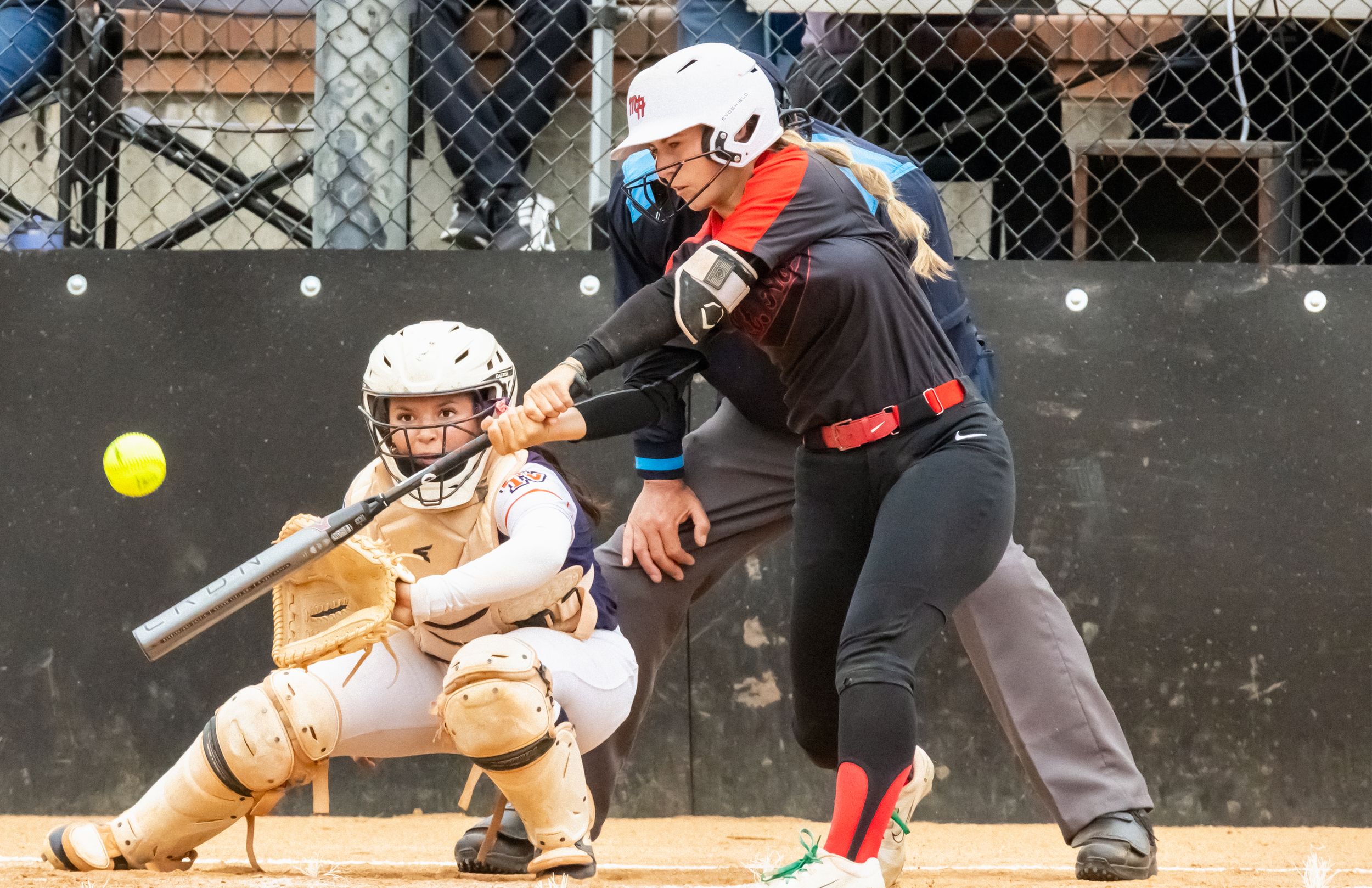 Softball batter swings at a pitch while the catcher and umpire watch behind home plate.