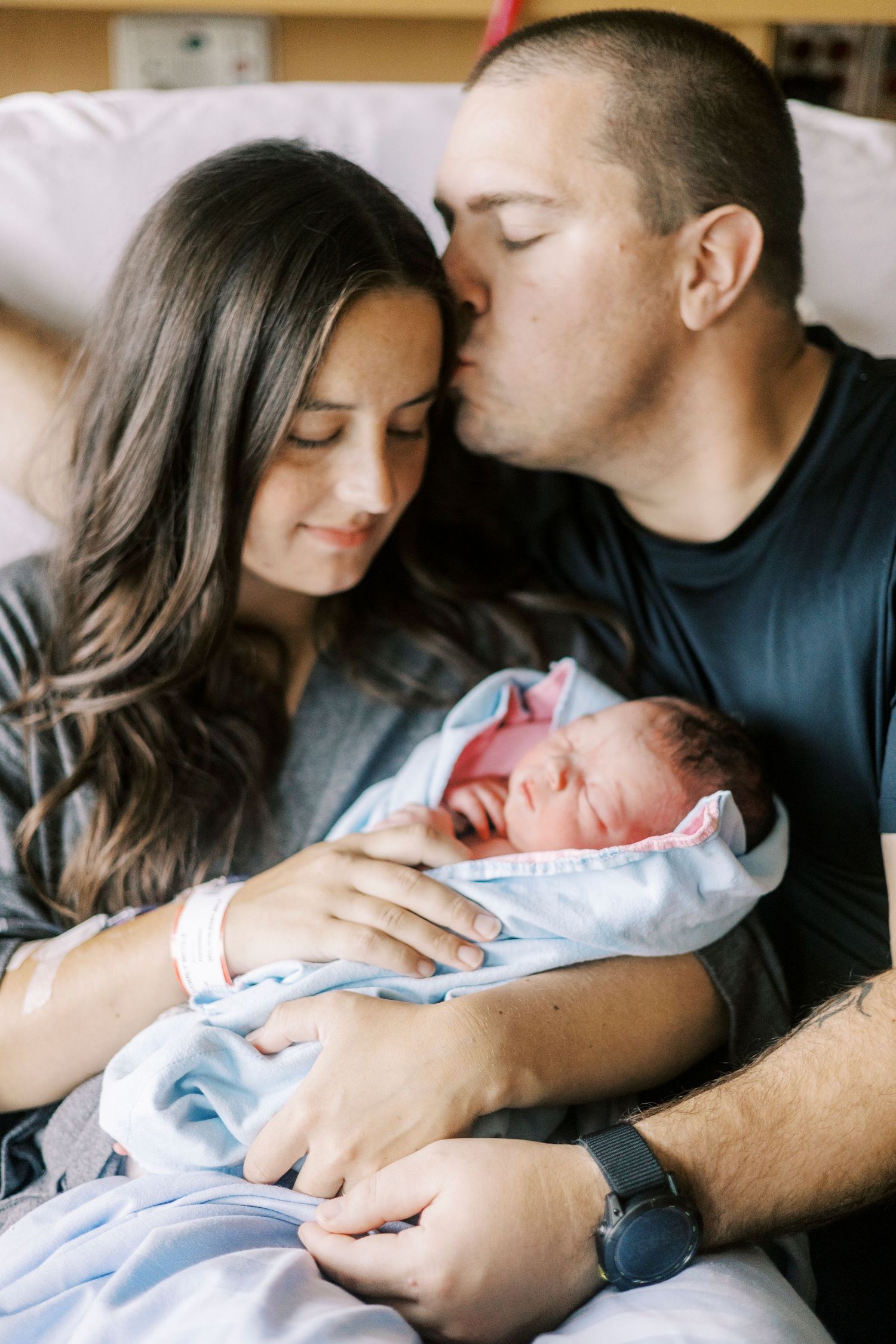 New parents share intimate moment with newborn baby wrapped in blue blanket.