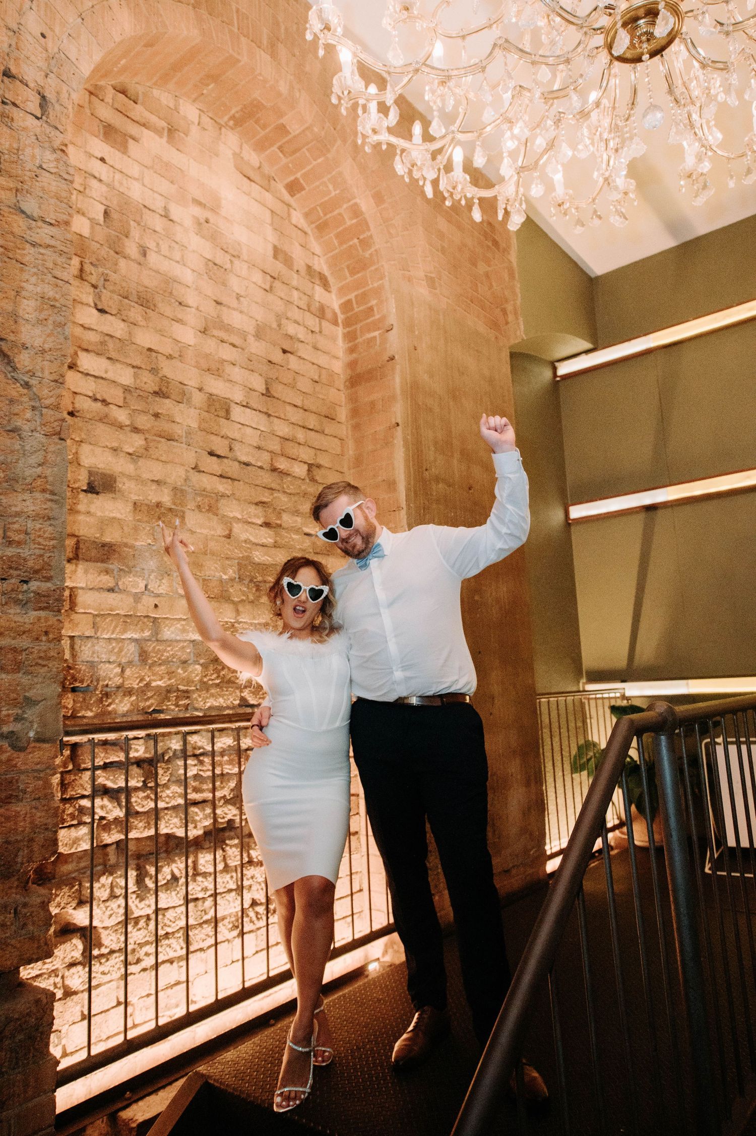 A couple celebrates in a rustic brick archway venue with a chandelier overhead.