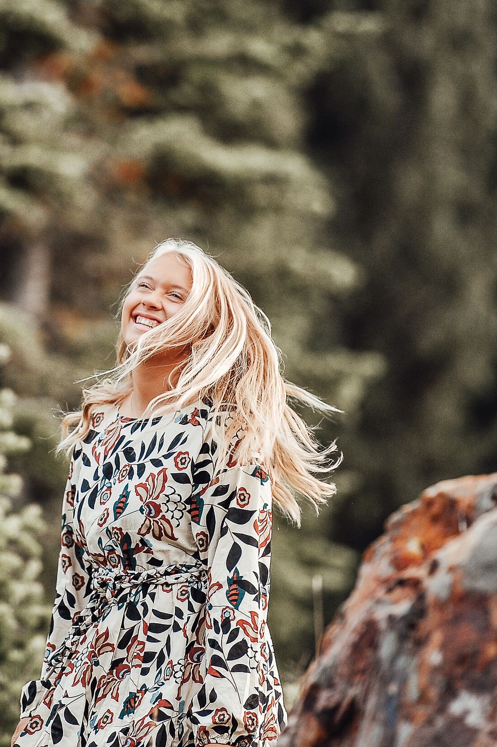 A floral print dress flows in the wind against an outdoor backdrop.