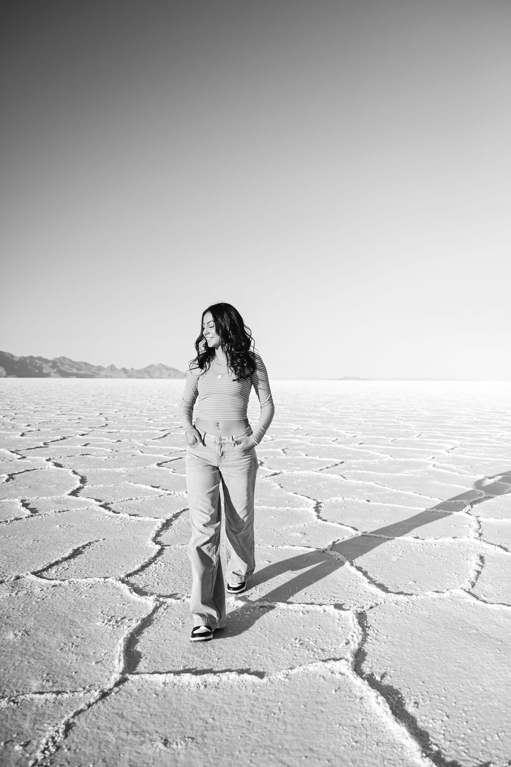 Figure walks across cracked salt flats in black and white photography.
