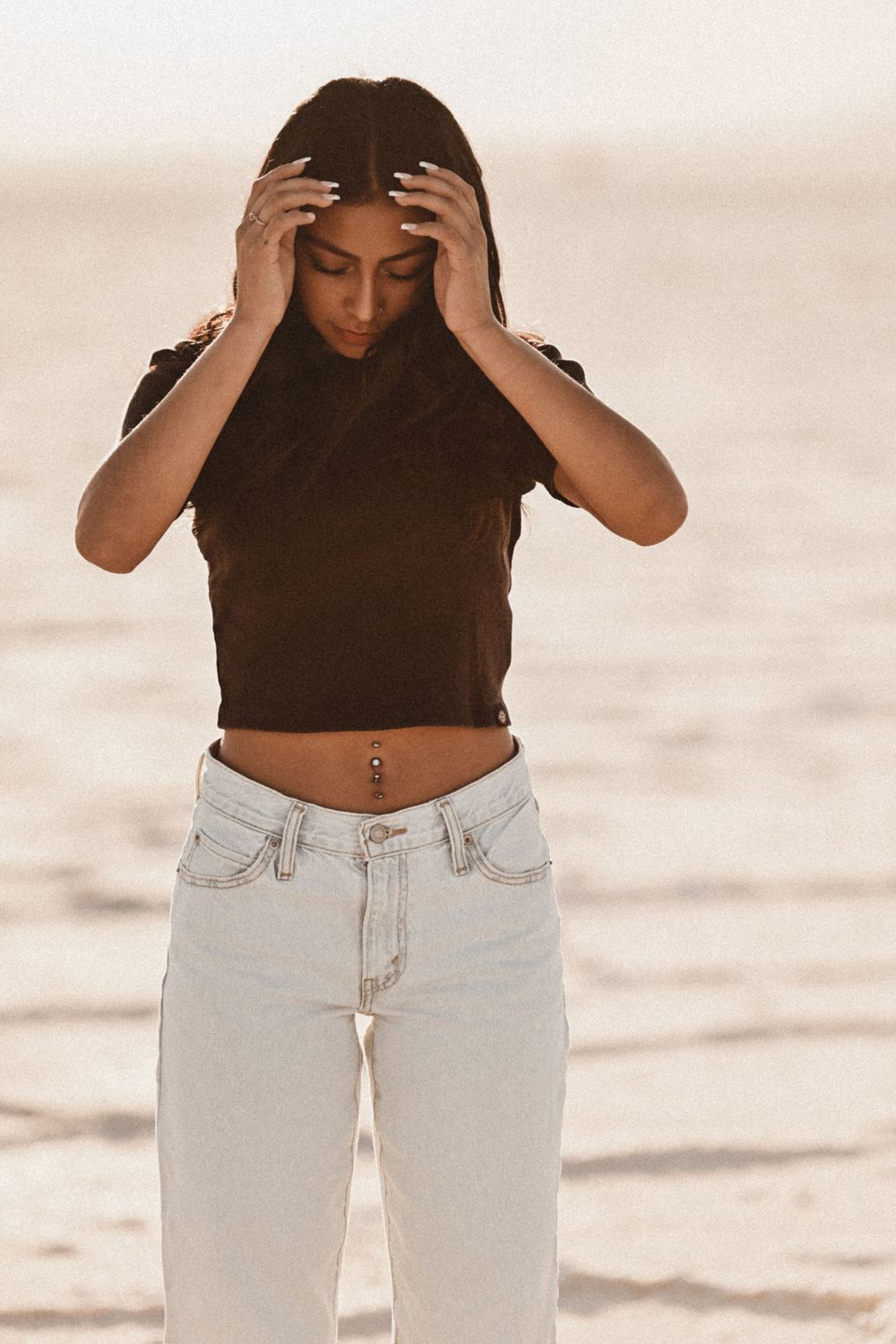 Woman in black top and light jeans poses emotively against white background.