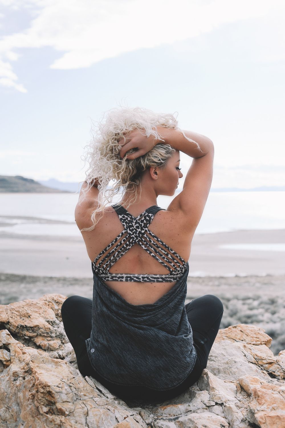 Person in polka dot top sits on coastal rocks overlooking water.