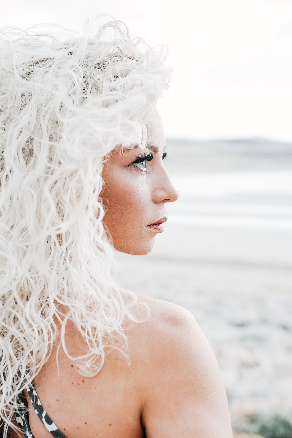 Artistic portrait with ethereal white hair and glitter makeup against bright background.