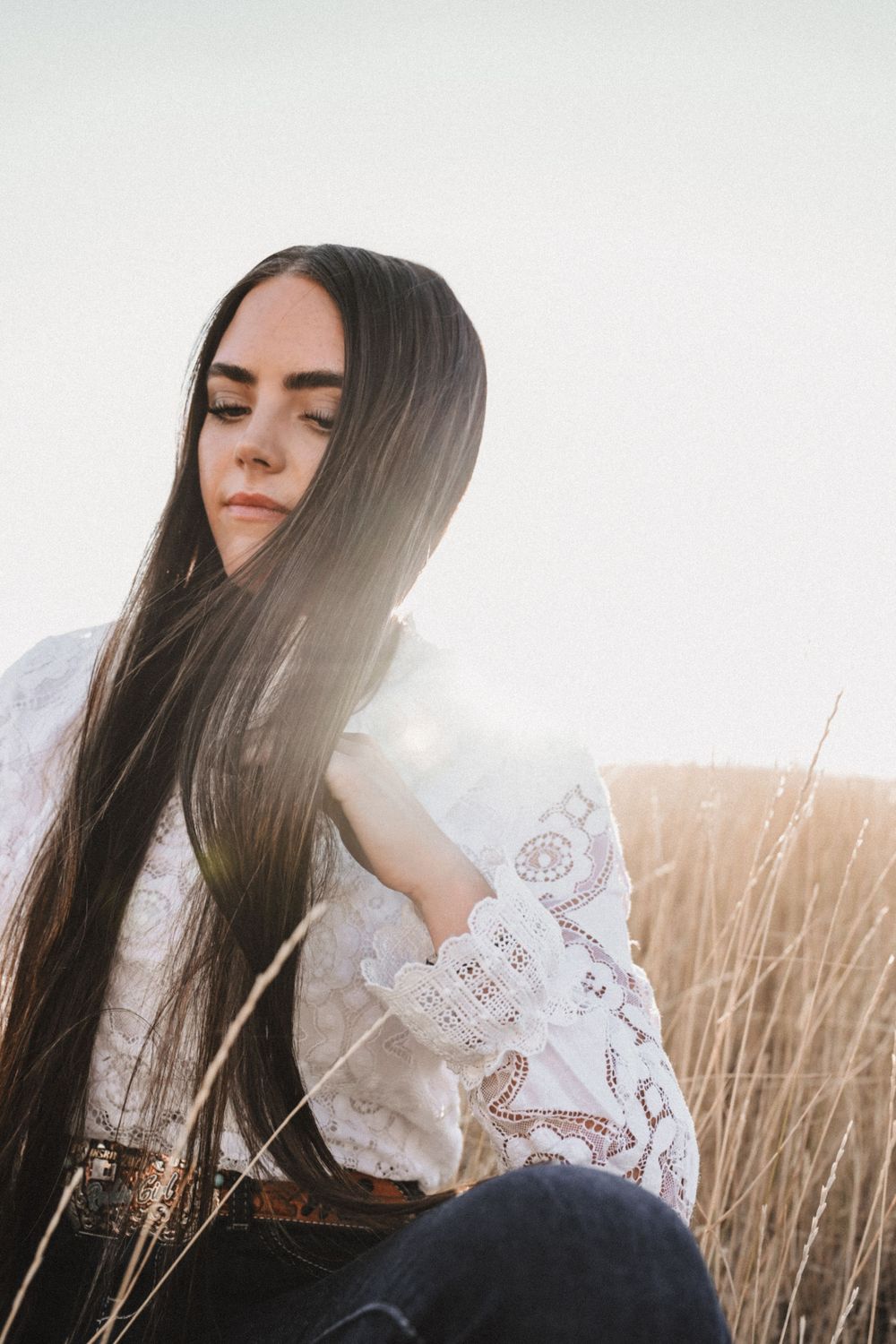Ethereal portrait in white lace dress sitting among sun-lit golden grass.