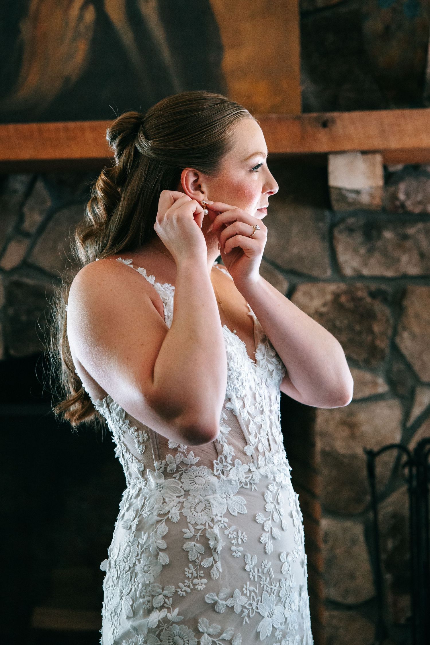 A bride in a white lace dress with floral appliques prepares for her wedding in front of a stone wall. Knoxville Photographer