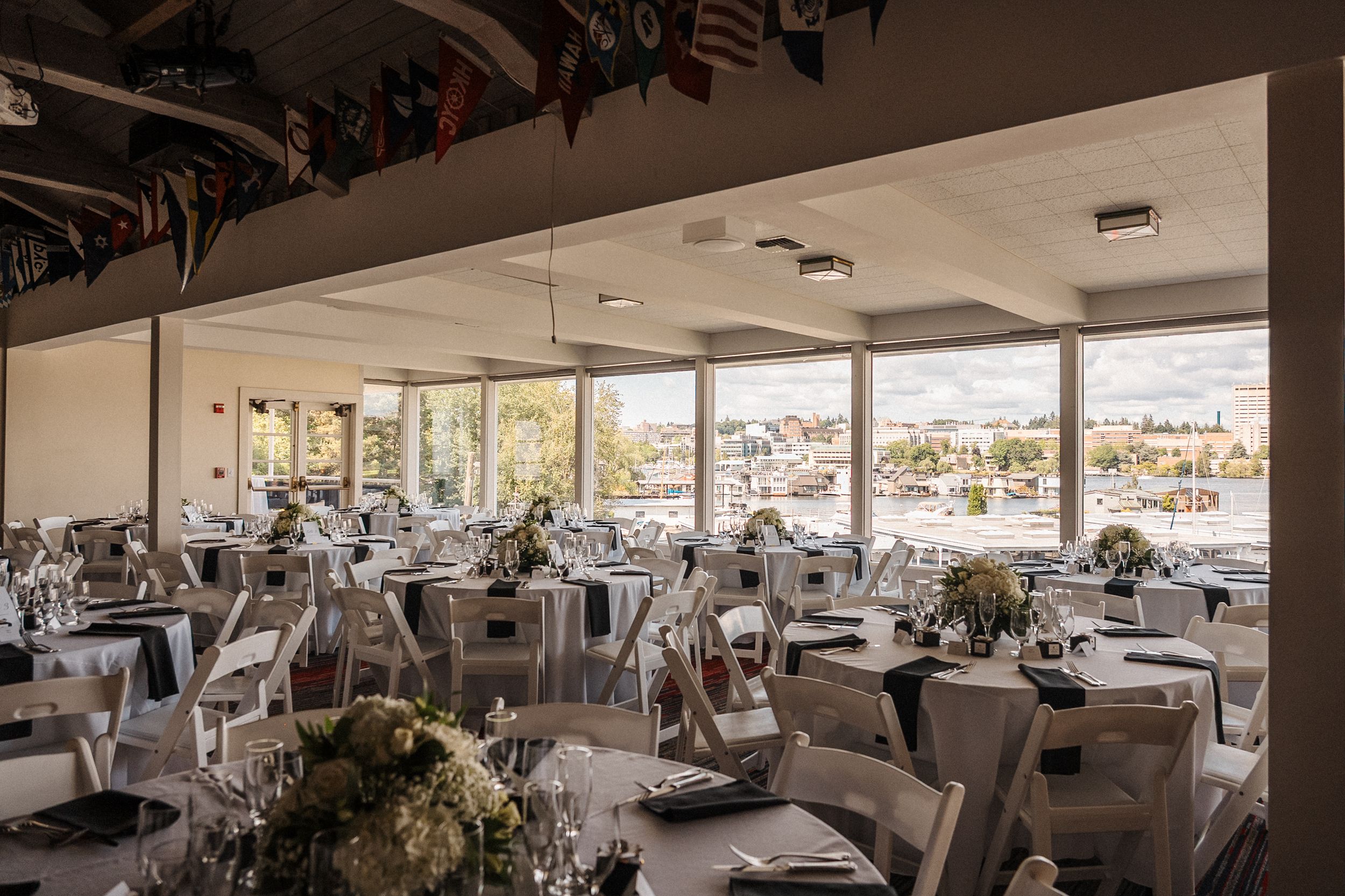 Modern restaurant interior with white tablecloths and panoramic waterfront views through large windows.