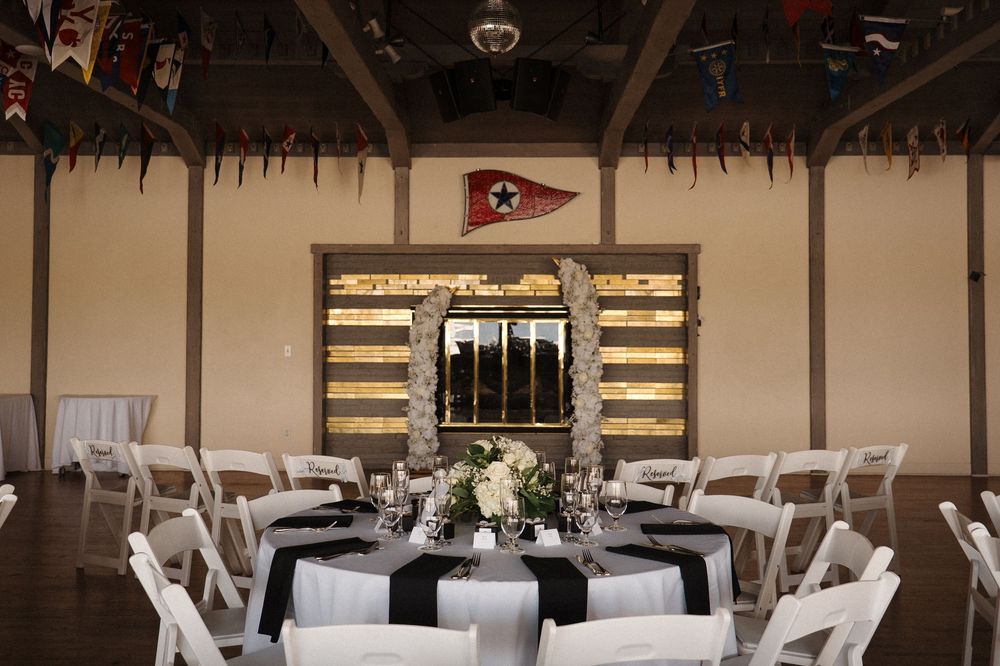 Modern ballroom with round dining tables, white chairs, and rustic wood wall panels lit by elegant chandeliers.