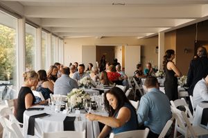Wedding guests mingle and celebrate at an elegant indoor reception with white tablecloths and natural lighting.