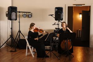 Professional audio speakers and equipment line the wall of an empty event space with wooden floors.