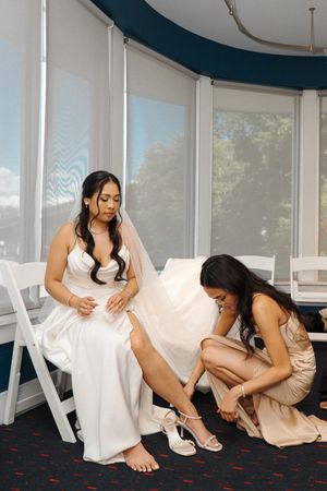 Wedding party members helping fit bridal shoes on couch.